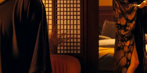 A young man and an elegant woman share a charged, intimate moment in a dimly lit modern living room.<a href=